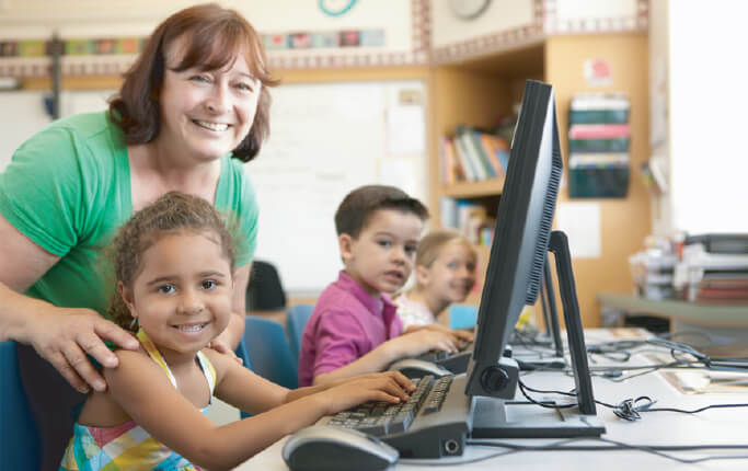 A speech therapist guiding elementary school students as they use computers to complete auditory processing tasks on the HearBuilder software.